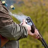 Un chasseur tire avec son fusil, des douilles s'envolent. La fumée s'échappe du choke du fusil.