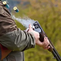 Un chasseur tire avec son fusil, des douilles s'envolent. La fumée s'échappe du choke du fusil.