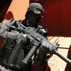 Un opérateur en tenue noire, masque et lunettes, tient un HK UMP 9. Fiche technique de cette arme compacte.