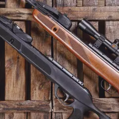 Deux carabines à plomb, l'une noire et l'autre en bois, reposent sur des lattes de bois. Le ressort de la carabine à plomb 30 joules est prêt à l'action.