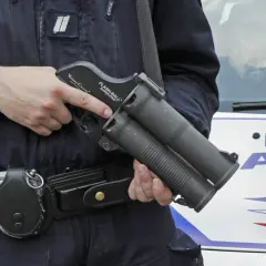 Un policier tient un lanceur flashball, arme non létale, près d'une voiture de police.