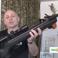 Un homme présente une carabine à air comprimé de 20 joules, avec des trophées de chasse en arrière-plan.