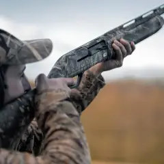 Chasseur en tenue camouflage, prêt à tirer avec ce qui semble être le meilleur fusil de chasse petit gibier.