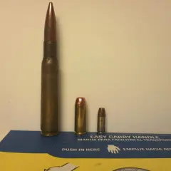 Trois cartouches de tailles différentes, dont une imposante de calibre 50 en mm, posées sur une boîte bleue et jaune.