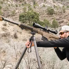 Un tireur d'élite ajuste son Barrett 50 munition sur un trépied, prêt à tirer dans un paysage désertique.