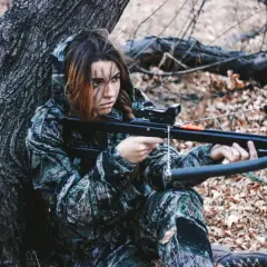 Jeune femme en tenue de camouflage, concentrée, prête pour la chasse à l'arbalète dans une forêt automnale.