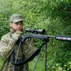 Chasseur en camouflage, prêt à l'action avec sa carabine A-Tec, la meilleure carabine pour battue sanglier, dans un sous-bois dense.
