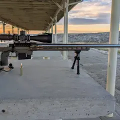 Fusil de précision prêt pour le tir, avec une cartouche .338 Lapua Magnum à portée de main. Le soleil se couche sur le champ de tir.