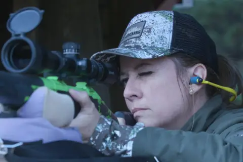 Femme concentrée visant avec un fusil de chasse, prête pour le bruit du tir.