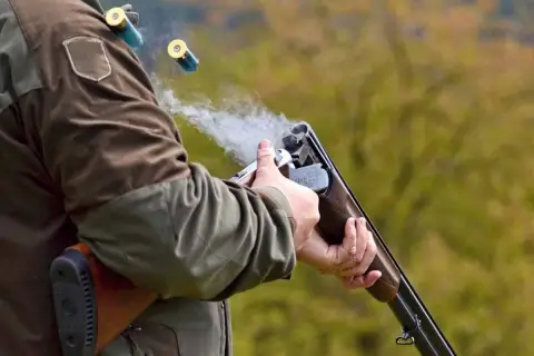 Un chasseur tire avec son fusil, des douilles s'envolent. La fumée s'échappe du choke du fusil.