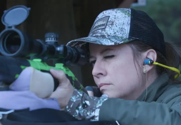 Femme concentrée visant avec un fusil de chasse, prête pour le bruit du tir.