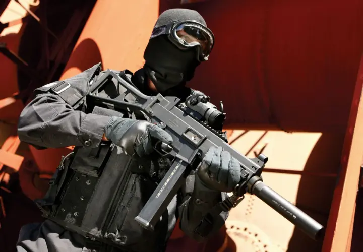 Un opérateur en tenue noire, masque et lunettes, tient un HK UMP 9. Fiche technique de cette arme compacte.