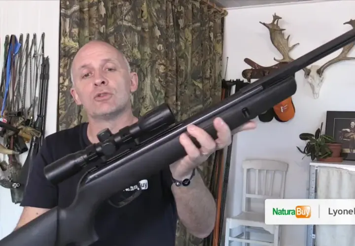 Un homme présente une carabine à air comprimé de 20 joules, avec des trophées de chasse en arrière-plan.