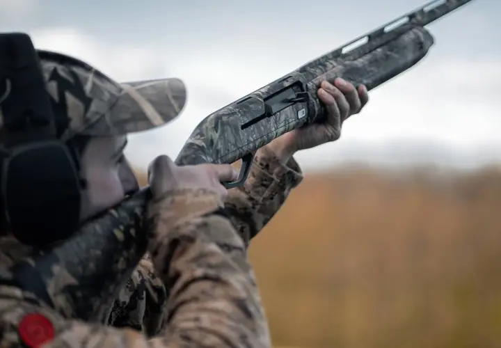 Chasseur en tenue camouflage, prêt à tirer avec ce qui semble être le meilleur fusil de chasse petit gibier.
