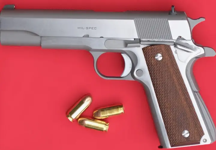 Un pistolet MIL-SPEC argenté avec des plaquettes de crosse en bois et trois cartouches à blanc à côté.
