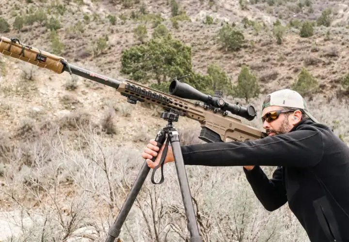 Un tireur d'élite ajuste son Barrett 50 munition sur un trépied, prêt à tirer dans un paysage désertique.