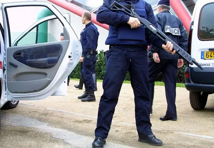 Un policier national tient un fusil à pompe, prêt à intervenir.