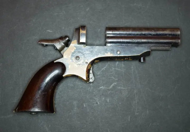 Un vieux derringer 22lr à double canon, avec une poignée en bois sombre et un mécanisme visible.