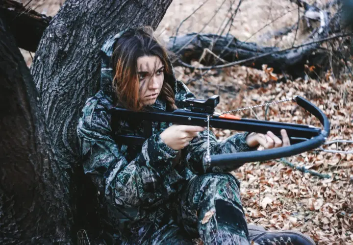Jeune femme en tenue de camouflage, concentrée, prête pour la chasse à l'arbalète dans une forêt automnale.