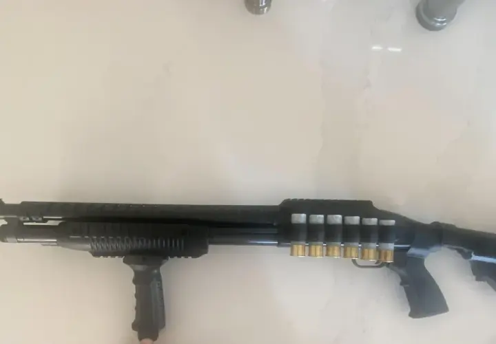 Un fusil Maverick 88 tactique, noir, avec une poignée avant, un rail supérieur et des cartouches dorées visibles sur le côté.