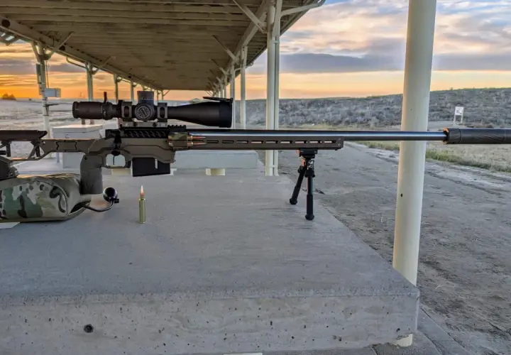 Fusil de précision prêt pour le tir, avec une cartouche .338 Lapua Magnum à portée de main. Le soleil se couche sur le champ de tir.