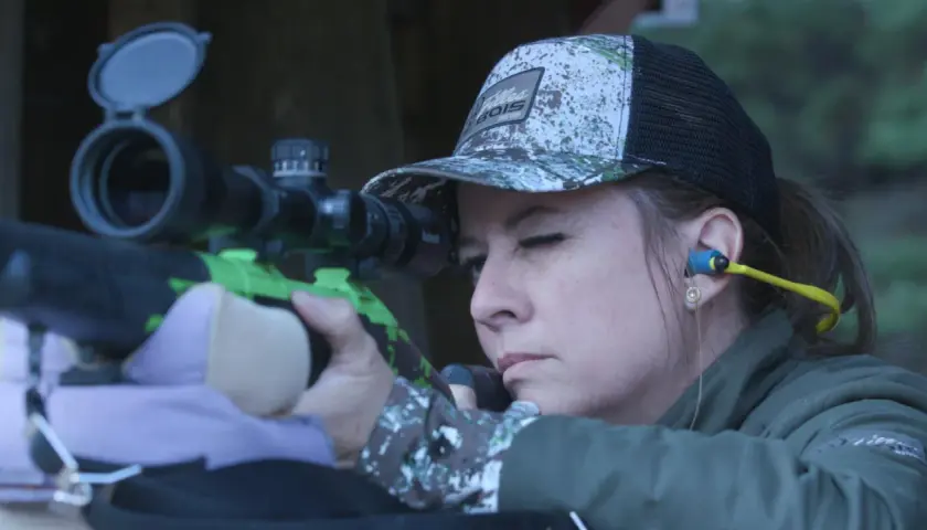 Femme concentrée visant avec un fusil de chasse, prête pour le bruit du tir.