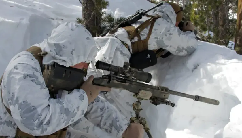 Deux snipers américains en tenue de camouflage hivernal se positionnent dans la neige, l'un visant avec son fusil sniper américain.