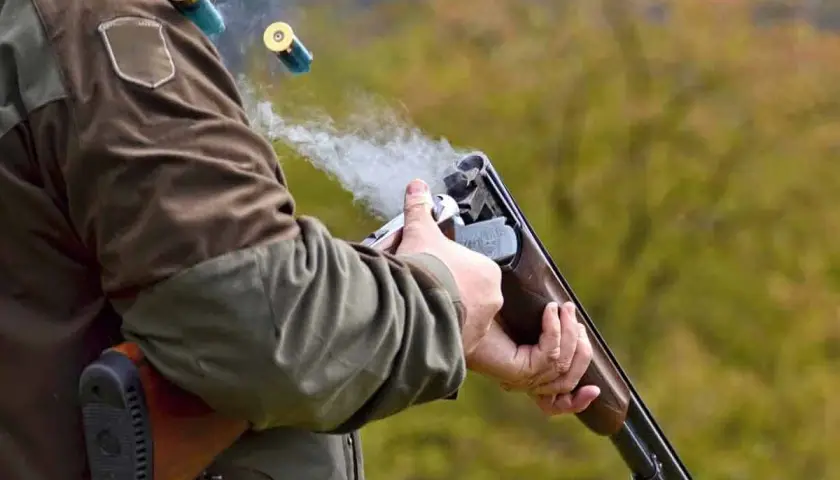 Un chasseur tire avec son fusil, des douilles s'envolent. La fumée s'échappe du choke du fusil.