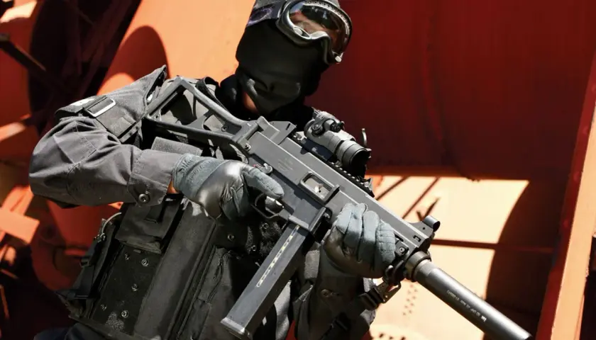 Un opérateur en tenue noire, masque et lunettes, tient un HK UMP 9. Fiche technique de cette arme compacte.