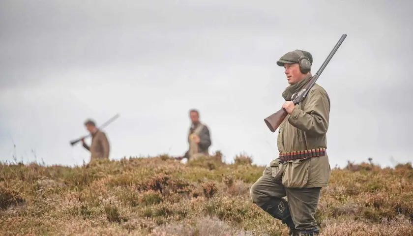 Chasseurs en tenue, fusils à l'épaule, dans un paysage de landes. L'interdiction du plomb tir sportif est une préoccupation croissante.