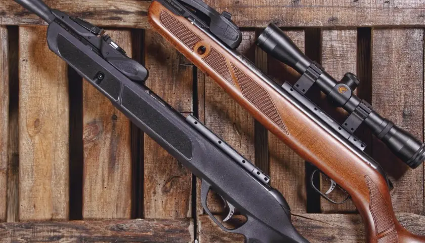 Deux carabines à plomb, l'une noire et l'autre en bois, reposent sur des lattes de bois. Le ressort de la carabine à plomb 30 joules est prêt à l'action.