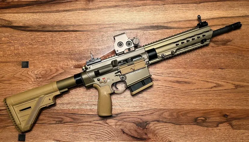 Un fusil HK MR308 couleur sable, avec lunette, repose sur un fond en bois.