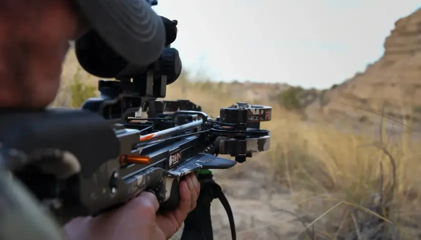 Chasseur visant avec une arbalète moderne, testant sa puissance en joule dans un paysage aride.