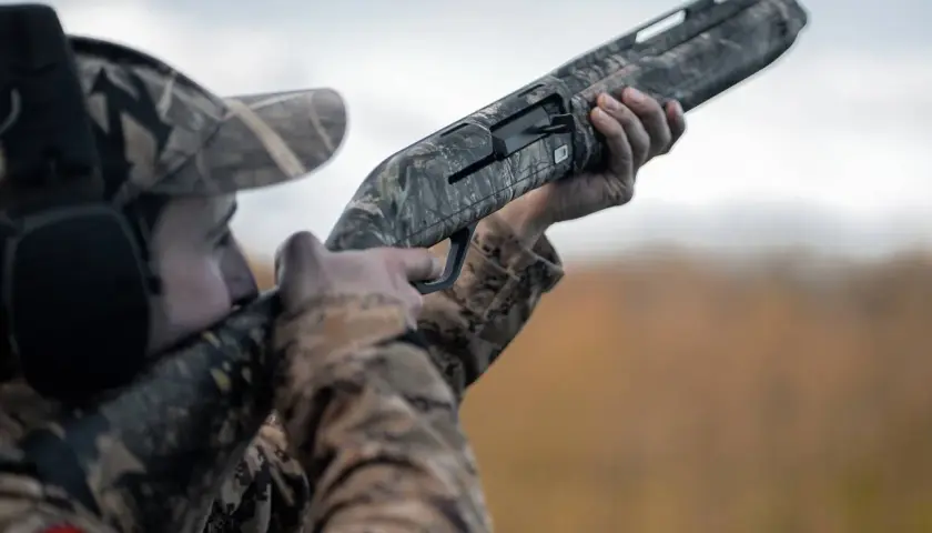Chasseur en tenue camouflage, prêt à tirer avec ce qui semble être le meilleur fusil de chasse petit gibier.