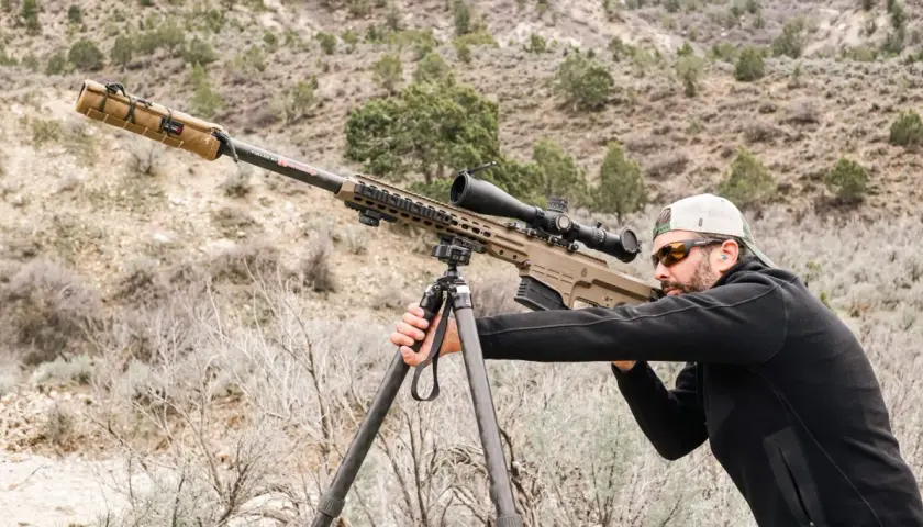 Un tireur d'élite ajuste son Barrett 50 munition sur un trépied, prêt à tirer dans un paysage désertique.