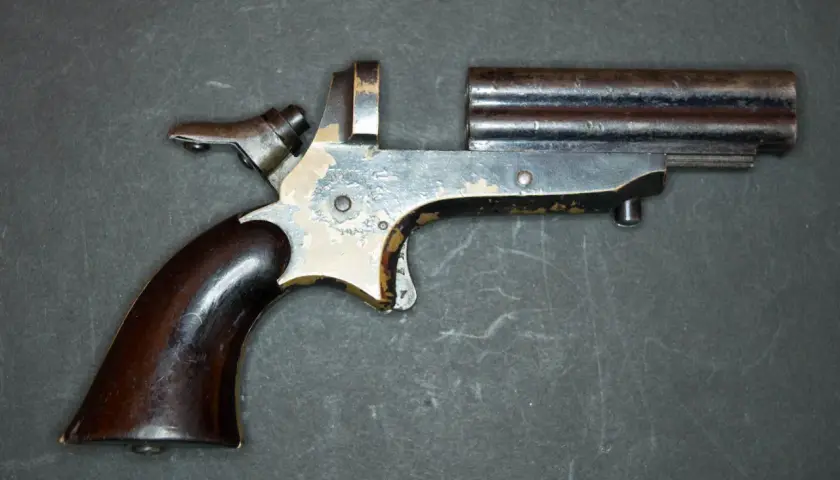 Un vieux derringer 22lr à double canon, avec une poignée en bois sombre et un mécanisme visible.