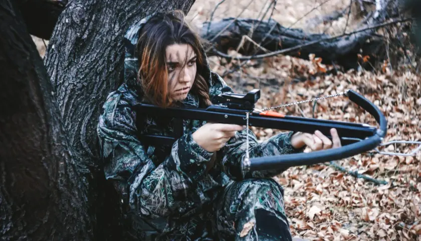 Jeune femme en tenue de camouflage, concentrée, prête pour la chasse à l'arbalète dans une forêt automnale.