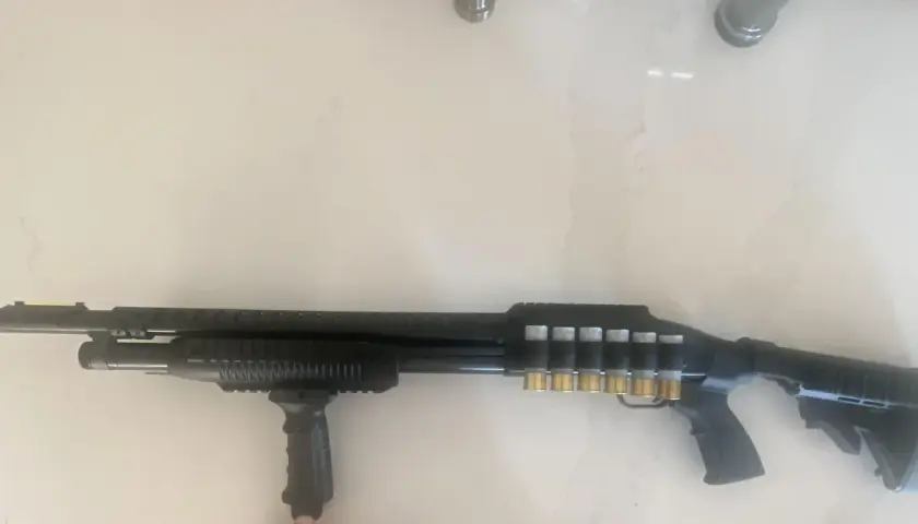 Un fusil Maverick 88 tactique, noir, avec une poignée avant, un rail supérieur et des cartouches dorées visibles sur le côté.