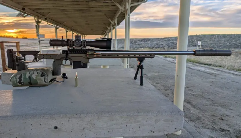 Fusil de précision prêt pour le tir, avec une cartouche .338 Lapua Magnum à portée de main. Le soleil se couche sur le champ de tir.