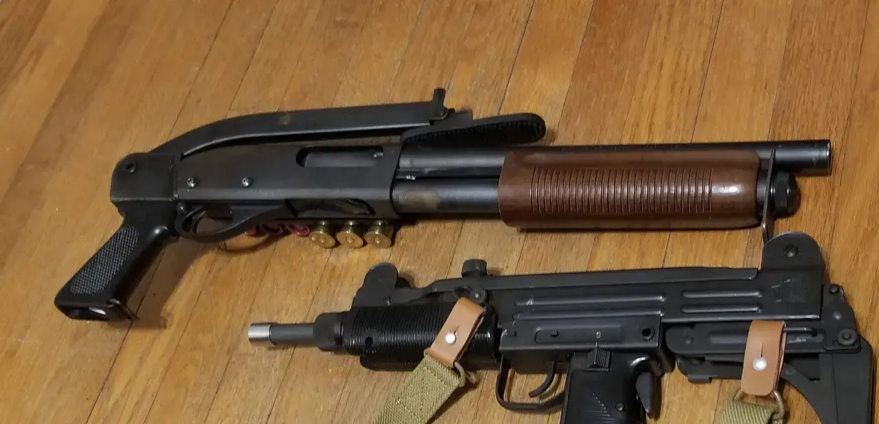 Un fusil à pompe riot gun et un pistolet-mitrailleur Uzi reposent sur un plancher en bois.
