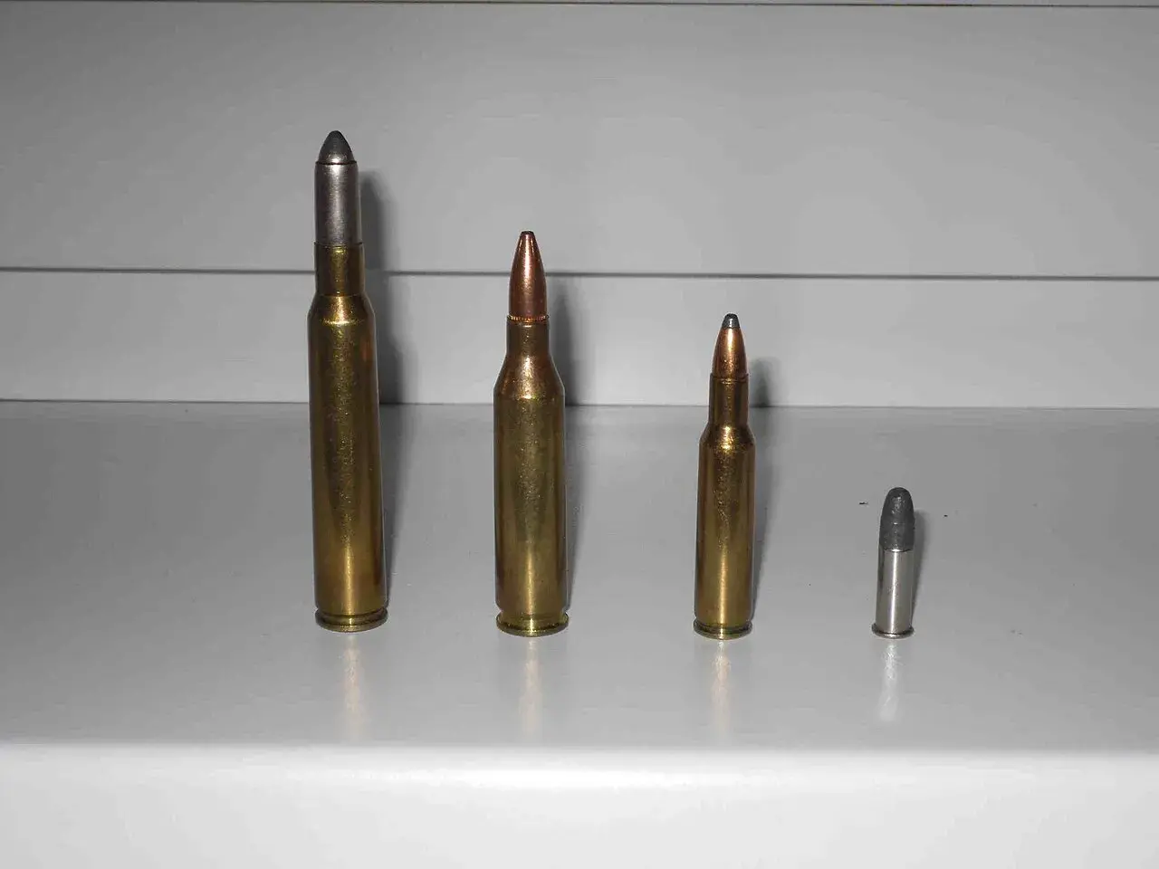Comparaison de munitions : une cartouche 222 Remington à gauche, une 223 Remington au centre, et deux plus petites à droite.
