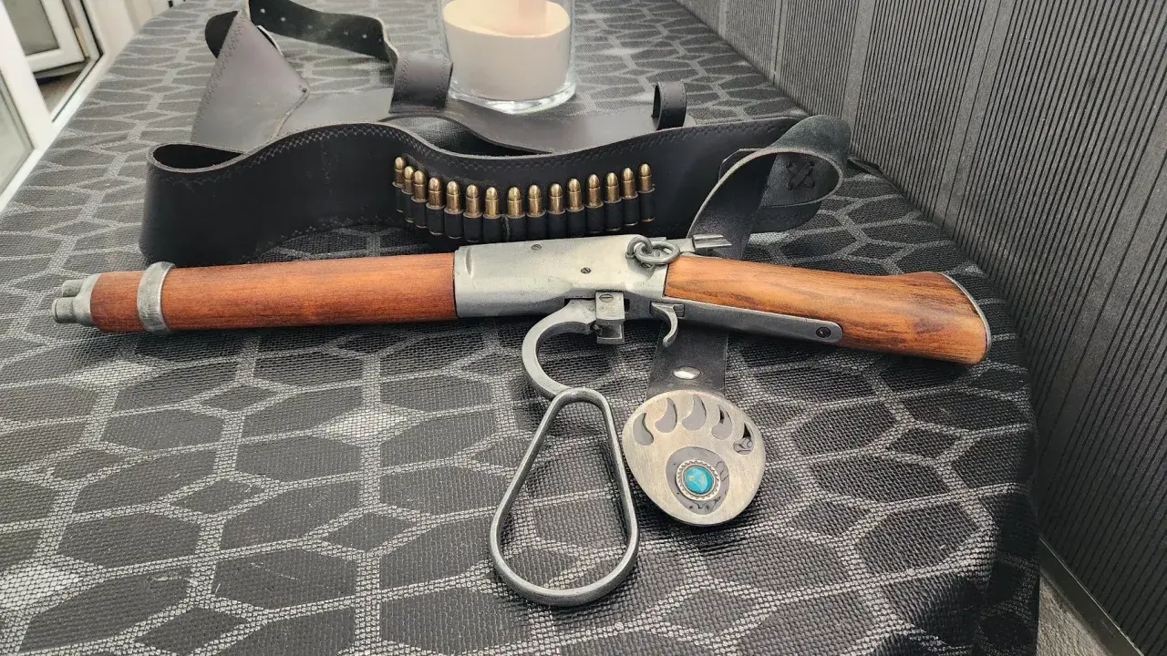 Carabine à levier sous garde en bois et métal, avec ceinture de munitions et boucle d'ours.