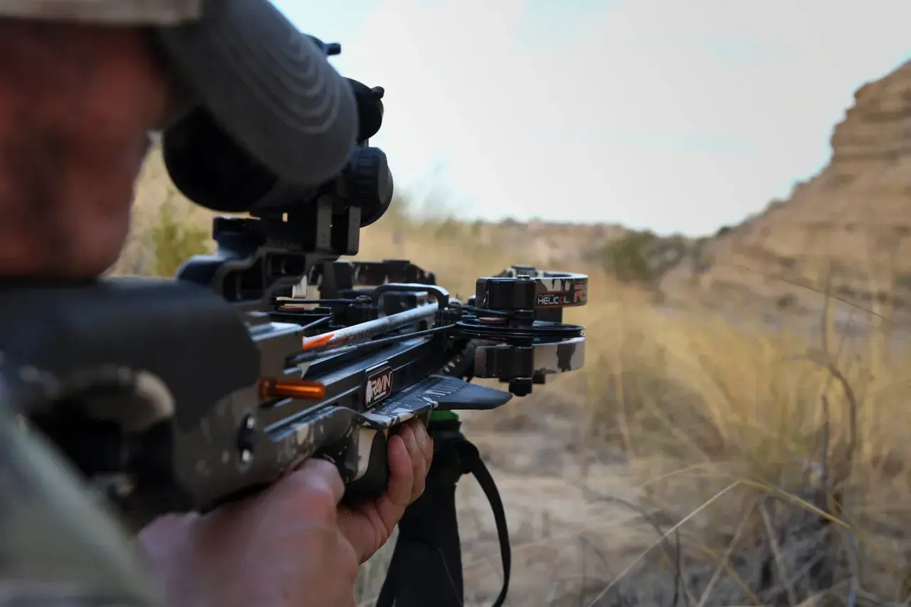 Chasseur visant avec une arbalète moderne, testant sa puissance en joule dans un paysage aride.