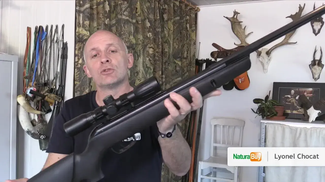 Un homme présente une carabine à air comprimé de 20 joules, avec des trophées de chasse en arrière-plan.