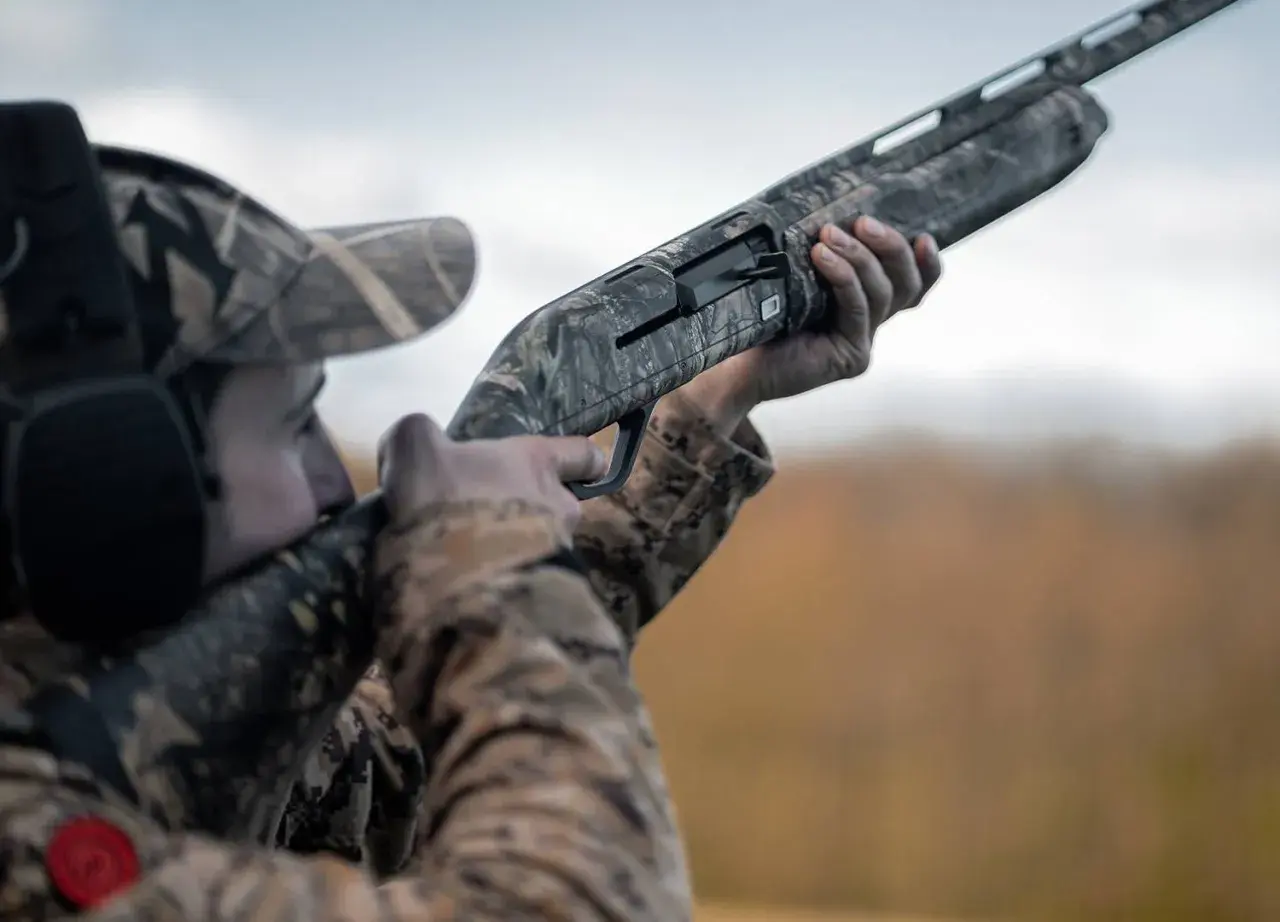 Chasseur en tenue camouflage, prêt à tirer avec ce qui semble être le meilleur fusil de chasse petit gibier.