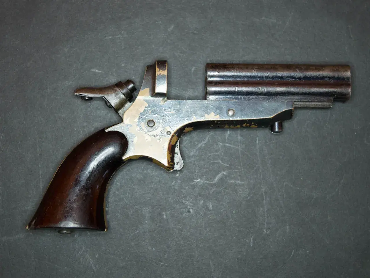 Un vieux derringer 22lr à double canon, avec une poignée en bois sombre et un mécanisme visible.
