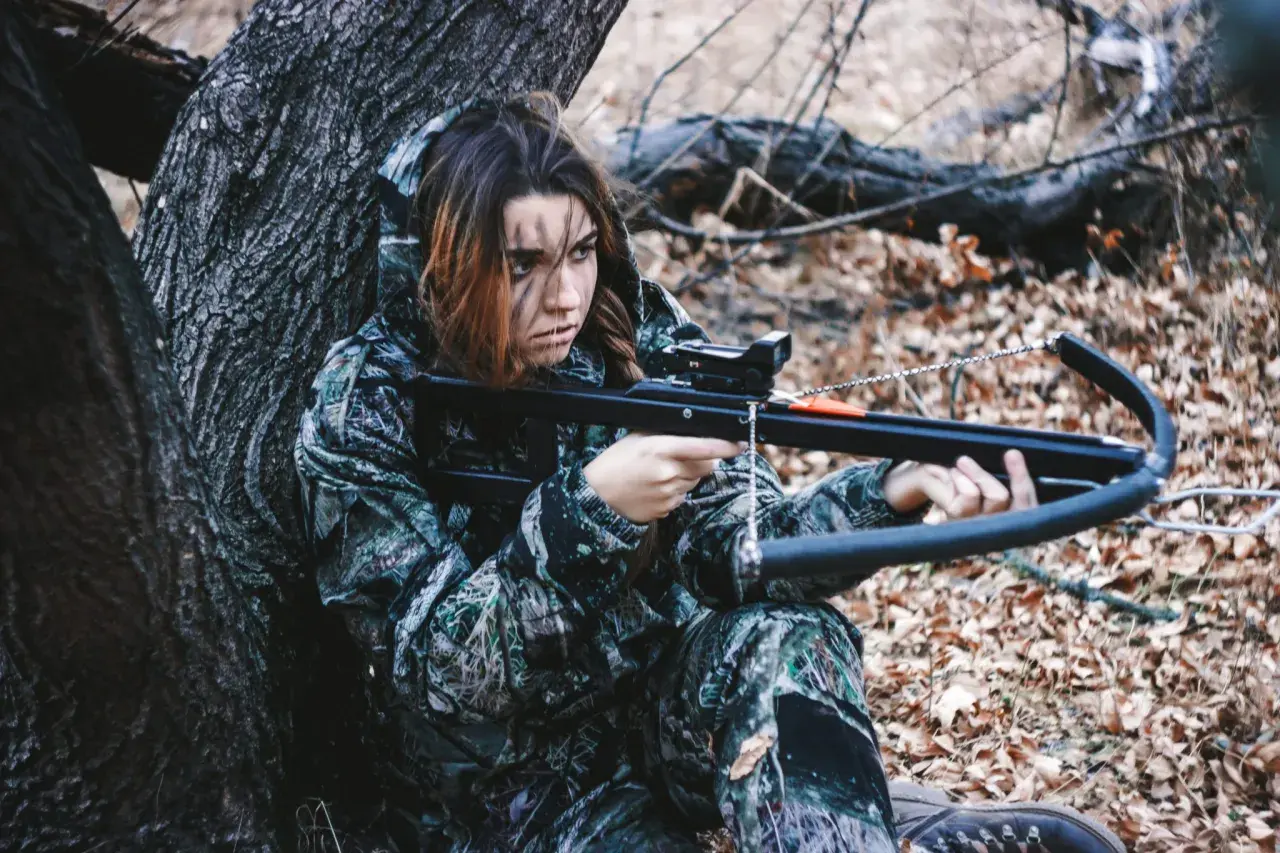 Jeune femme en tenue de camouflage, concentrée, prête pour la chasse à l'arbalète dans une forêt automnale.