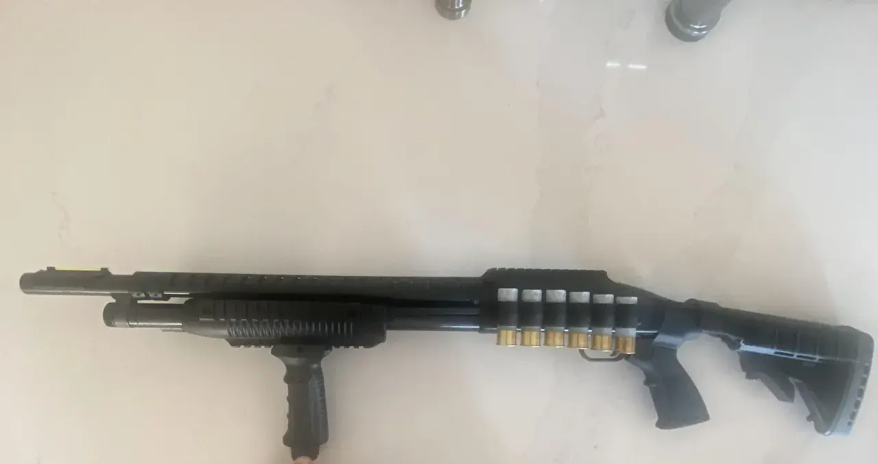 Un fusil Maverick 88 tactique, noir, avec une poignée avant, un rail supérieur et des cartouches dorées visibles sur le côté.