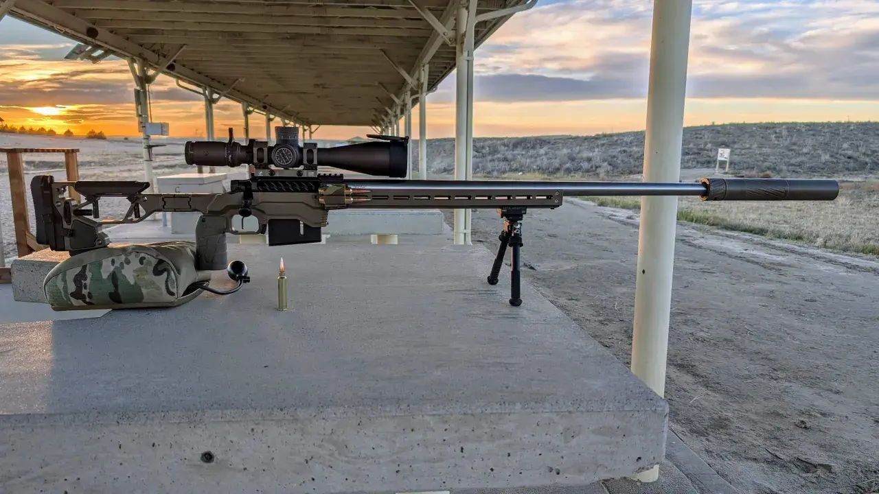 Fusil de précision prêt pour le tir, avec une cartouche .338 Lapua Magnum à portée de main. Le soleil se couche sur le champ de tir.