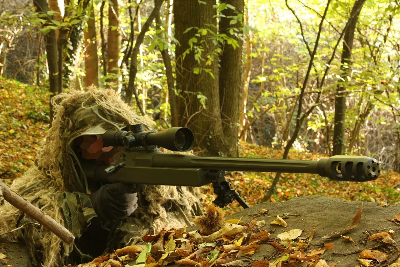 Un tireur d'élite camouflé dans les bois, tenant un fusil Macmillan.